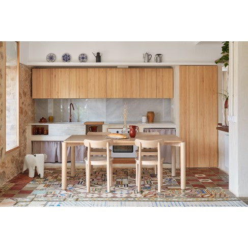 Modern kitchen with wooden cabinets, table, and chairs on a patterned floor.