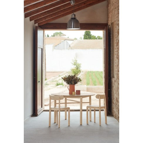 Dining area with a round table and chairs in a room with wooden beams and large windows.